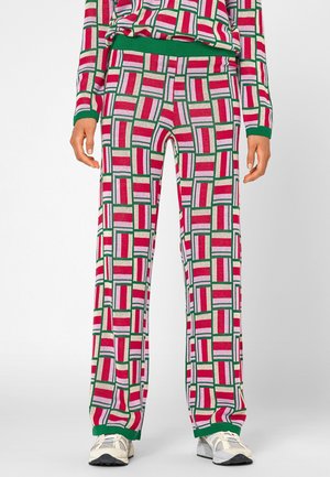 Personne portant un pantalon et un haut assortis avec des blocs géométriques rouges, roses, blancs et verts, avec une bordure verte, assortis à des baskets blanches.