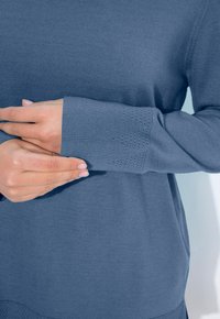 Sininen neulepaita, jossa on ribbireunat ja tekstuuripinta. Kangas näyttää pehmeältä ja mukavalta, ja se on rentoa mallia.