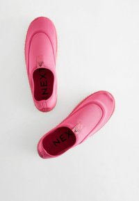 Rosa Slipper mit einem glatten Textilobermaterial, rutschfester Sohle und einem kleinen Logo-Patch an der Ferse. Rundes Toe-Design, minimalistischer Stil.