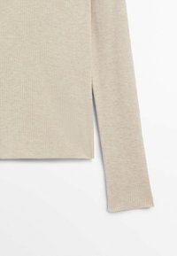 Light beige ribbed long-sleeve top featuring side slits at the hem. The fabric has a soft texture with a fitted design.