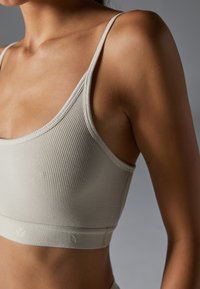 Geribbeld, lichtgrijze bralette met dunne bandjes en een aansluitend ontwerp. Heeft een zachte textuur en een subtiele logo op de elastische band.