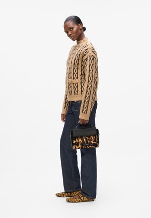 Beige knitted sweater with a cable pattern, black stripes, and gold buttons on the shoulder. Dark blue jeans and leopard-print shoes. Black and leopard handbag.