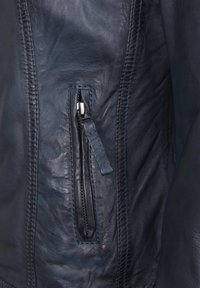 Mörkblå läderjacka med en vertikal dragkedjeficka, sydda detaljer och en mjuk yta, som betonar hållbarhet och design.