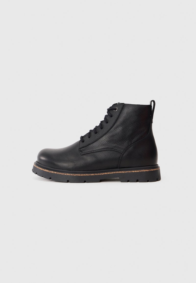 Bottine en cuir noir avec tige texturée, devant à lacets, languette à l'arrière, semelle épaisse en caoutchouc avec bordure beige, sur fond gris clair.