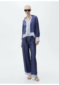 Camicia a maniche lunghe a righe navy e bianche con accenti blu abbinata a pantaloni a gamba larga coordinati. Il materiale sembra leggero e liscio.