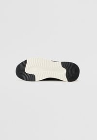 Semelle de sneaker noire et blanche avec un design texturé. Comprend des rainures prononcées sur le caoutchouc noir et une semelle intermédiaire blanche lisse.