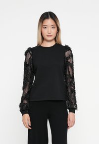 Sudadera negra con mangas largas transparentes adornadas con flores en negro. El cuerpo es de tela sólida, con mangas largas que tienen acentos de tela texturizada.