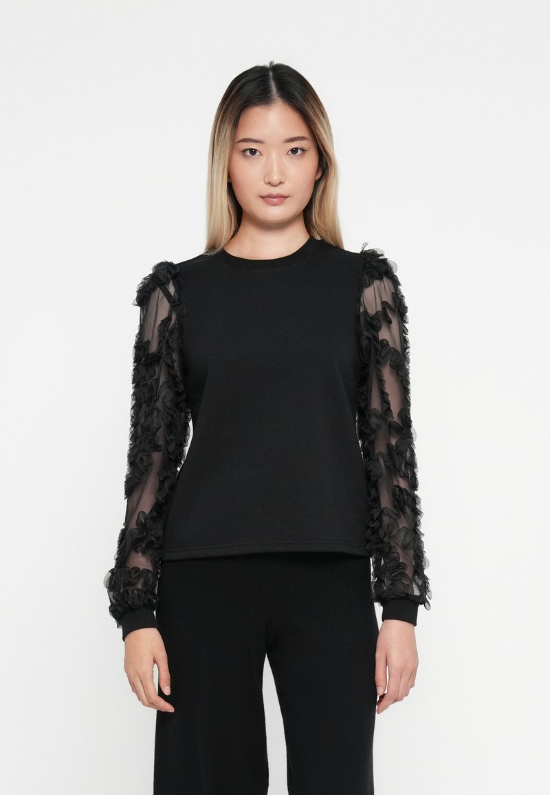 Sudadera negra con mangas largas transparentes adornadas con flores en negro. El cuerpo es de tela sólida, con mangas largas que tienen acentos de tela texturizada.