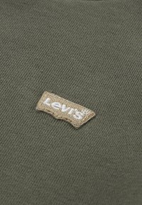 Tessuto verde oliva con una superficie texturizzata; presenta un'etichetta tessuta beige con "Levi's" ricamato in bianco.
