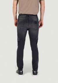 Jeans noirs skinny avec une finition délavée, dotés de deux poches arrière et d'une petite étiquette de marque sur la poche droite, portés avec des baskets noires.