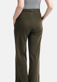 Olijfgroene, wijde broek van zachte stof met een elastische tailleband en zijzakken, weergegeven vanuit de achteraanzicht.