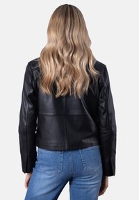 Black leather jacket with a cropped design, smooth texture, and long sleeves. Worn over light blue denim jeans, showing a back view.