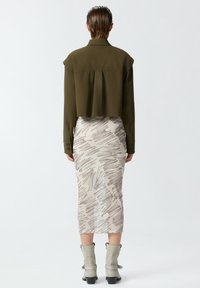 Camicia verde oliva tagliata, gonna midi a fantasia beige chiaro con dettagli testurizzati e stivaletti grigi alla caviglia con tacco a blocco.