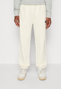 Cremefarvede sweatpants med elastisk talje og manchetter, med et lille broderet logo på venstre ben. Båret med lyse sneakers.