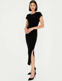 Czarna dopasowana sukienka z krótkimi bufkami, rozcięciem do kolan i elegancką sylwetką. Połączona z czarnymi, szpiczastymi szpilkami na formalny wygląd.