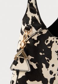 Borsa a tracolla a stampa mucca bianca e nera con una texture morbida, hardware dorato e un'etichetta triangolare decorativa sul lato.