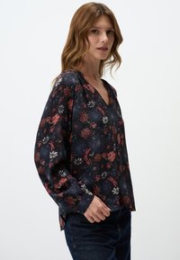 Blusa floreale con scollatura a V, maniche lunghe e uno sfondo scuro. Presenta fiori rossi, bianchi e blu, con una vestibilità ampia e spacchi laterali.