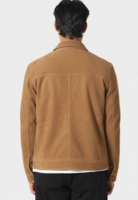 Brązowa zamszowa kurtka o luźnym kroju, z rozkładanym kołnierzem, mankietami zapinanymi na guziki oraz przeszyciami z tyłu.