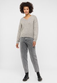 Jasnoszara sweter dzianinowy z dekoltem w serek i ściągaczami na rękawach, w połączeniu z wysokim stanem, wyblakłymi szarymi dżinsami o prostych nogawkach oraz czarnymi botkami.