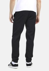 Czarne dresy wykonane z miękkiego materiału, cechujące się luźnym krojem, elastycznym pasem w talii i zwężanymi kostkami. Noszone z czarno-białymi trampkami.