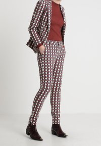 Geometrisch patroon kostuum met een aansluitende blazer en taps toelopende broek. Kenmerkt zich door een geometrisch ontwerp in rood, marineblauw en crème. Soepele stof met een gepolijste afwerking.