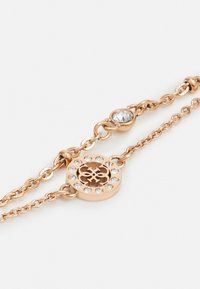 Rosa gullarmbånd med en sentral sirkulær pendel, prydet med klare edelstener og intrikat utskårent design. Justerbare kjedeledd.