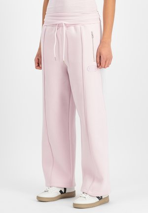 Pantaloni della tuta rosa chiaro a gamba larga con tasca laterale con cerniera, vita con coulisse e cuciture visibili, indossati con scarpe da ginnastica bianche e nere.