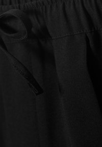 Cintura elástica negra con un detalle de cordón. La tela parece suave con un ligero brillo, mostrando una textura tejida.