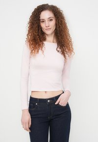 Ροζ ανοιχτόχρωμο crop top με μακριά μανίκια και τετράγωνο ντεκολτέ, σε συνδυασμό με σκούρο μπλε εφαρμοστά τζιν με πέντε τσέπες και κούμπωμα με κουμπί.