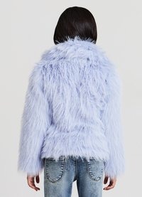 Hellblaue Kunstpelzjacke mit strukturierter Oberfläche, langen Ärmeln und figurbetonter Silhouette. Trägt hellblaue Jeans, Ansicht von hinten.