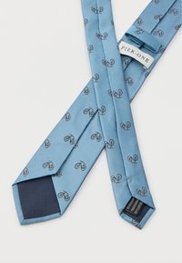 Ανοιχτό μπλε γραβάτα με επαναλαμβανόμενο μοτίβο μαύρων και κόκκινων ποδηλάτων, με ετικέτα Pier One, απλωμένη σε λευκό φόντο.