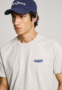 Gray, soft cotton t-shirt featuring a blue brushstroke logo. Paired with a navy cap displaying “Pepe Jeans” in white embroidery.