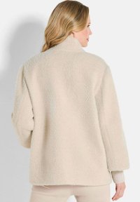 Beige fleece jas met een hoge kraag, textuurpatroon en geribde manchetten. Zacht materiaal met een ontspannen pasvorm en een licht gebogen zoom.