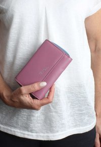 Pink leather wallet with a blue accent, rectangular shape, visible stitching, and embossed logo. Held in a hand against a white top.