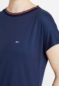 Granatowa bawełniana koszulka z krótkim rękawem, z żeberkowym dekoltem w czerwone i białe akcenty oraz małym logo na piersi. Luźny krój.