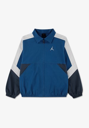 Blaue Zip-up-Jacke mit weißen und schwarzen schrägen Streifen an den Ärmeln, elastischen Bündchen und Saum sowie kleinem weißem Jumpman-Logo auf der Brust.