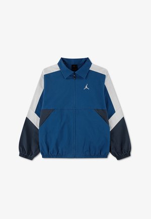 Blaue Zip-up-Jacke mit weißen und schwarzen schrägen Streifen an den Ärmeln, elastischen Bündchen und Saum sowie kleinem weißem Jumpman-Logo auf der Brust.