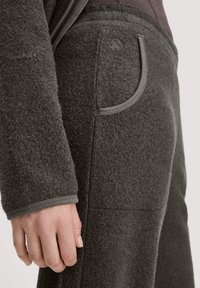 Dunkelgrauer Fleece-Stoff mit strukturierter Oberfläche, ausgestattet mit einer runden Tasche und gerippten Bündchen für zusätzlichen Detailreichtum und Struktur.