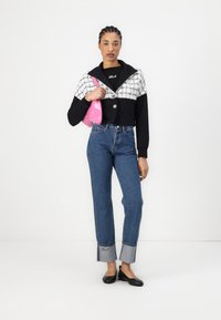 Black cropped sweater with white textured accents and button, paired with blue high-waisted jeans featuring cuffed hems. Model holds a pink bag.