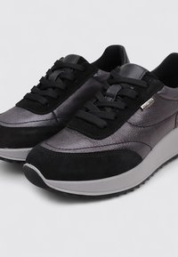 Zapatillas en negro y gris oscuro con una parte superior de cuero texturizado, detalles de ante, cordones planos y una gruesa suela de goma gris con patrones de tracción.