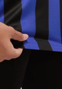 Modrý a černý pruhovaný atletický triko s plochým lemem, zobrazující ruku zvedající okraj. Hladká textura, lehká látka.