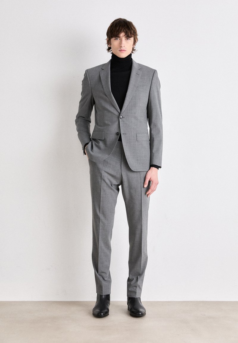 Completo grigio con vestibilità sartoriale, tessuto testurizzato, blazer a un bottone, abbinato a un dolcevita nero e stivali di pelle nera.