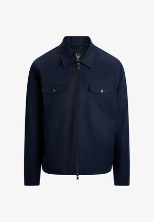 Marineblå jakke med glidelås, spiss krage, to brystlommer med knapper og lange ermer.