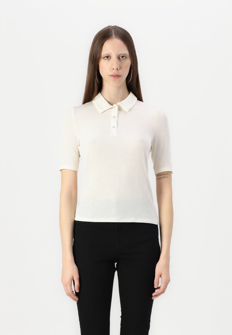 Rövid ujjú krémszínű polo póló gombos záródással, puha tapintással és slim fit kialakítással, fekete nadrággal párosítva.