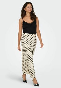 Sort blondertrimmet cami-top kombineret med en cremefarvet, satin maxi-nederdel med sort, prikket mønster. Bruges med sorte og hvide spidse hæle.