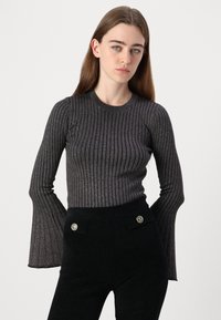 Haut en tricot côtelé noir avec des manches évasées, présentant un léger éclat. Associé à un pantalon noir taille haute avec des boutons décoratifs.