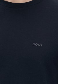 Prim-plan cu un tricou bleumarin cu guler rotund care prezintă cuvântul „BOSS” în litere mici, în relief, pe piept.
