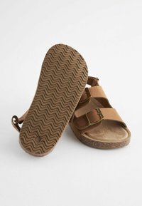 Bruna sandaler med två justerbara remmar, texturerad gummisula och en korkfotbädd. Utrustade med guldfärgade spännen för säker passform.