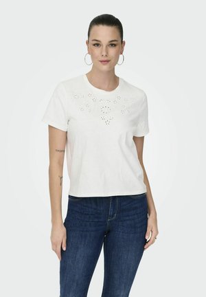 Witte katoenen t-shirt met korte mouwen, met uitsneden in bloemmotieven aan de voorkant en een relaxte pasvorm, gecombineerd met donkerblauwe jeans.