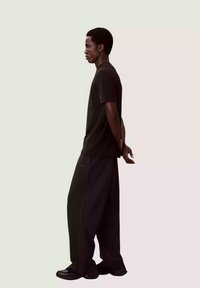 Czarny t-shirt z krótkim rękawem zestawiony z szerokimi czarnymi spodniami. Strój cechuje się luźnym krojem i subtelnymi detalami szwów. Całość dopełniają czarne sneakersy.